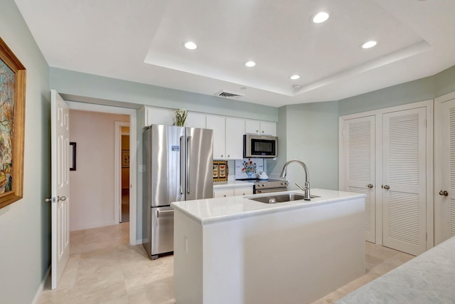 kitchen with an island with sink, sink, white cabinets, a raised ceiling, and appliances with stainless steel finishes