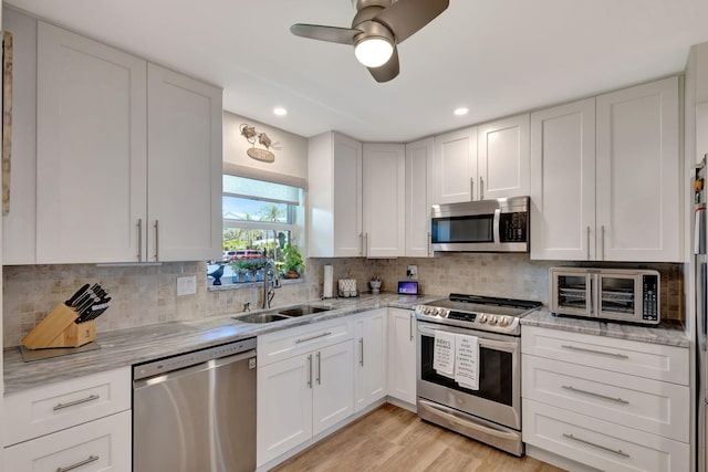 kitchen featuring light wood-type flooring, appliances with stainless steel finishes, backsplash, sink, and white cabinets