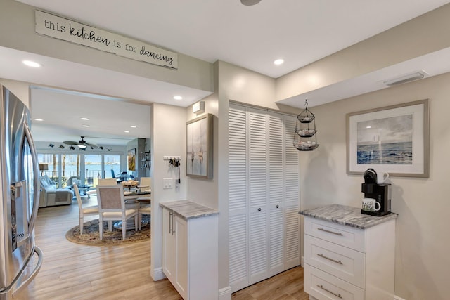 kitchen featuring light wood-type flooring, light stone countertops, stainless steel fridge, and white cabinets