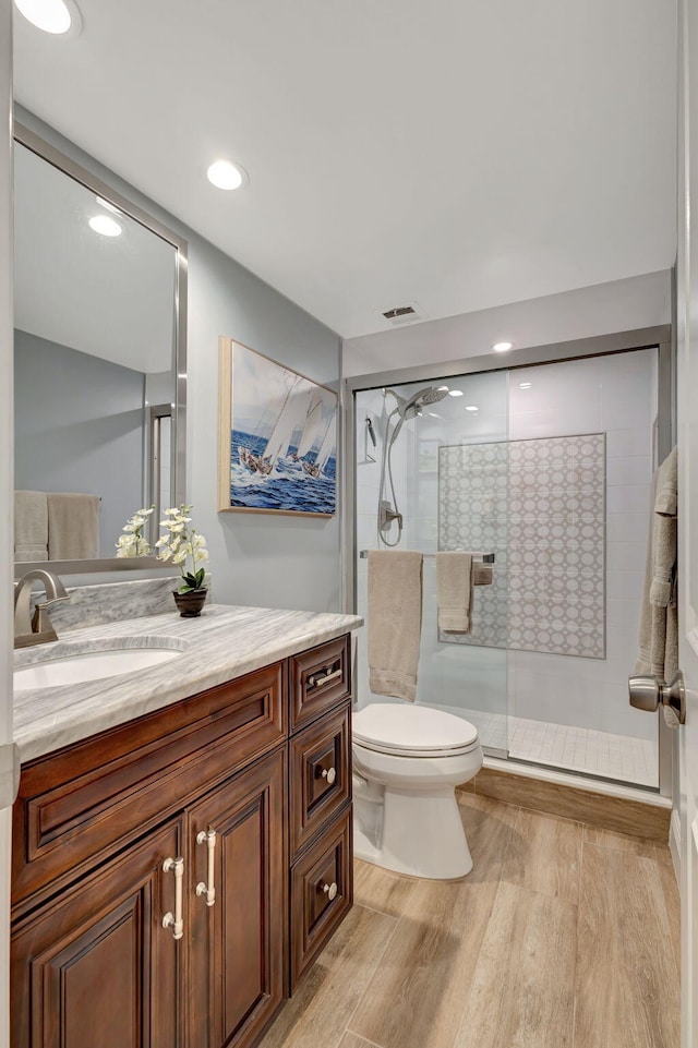 bathroom with wood-type flooring, vanity, toilet, and a shower with shower door