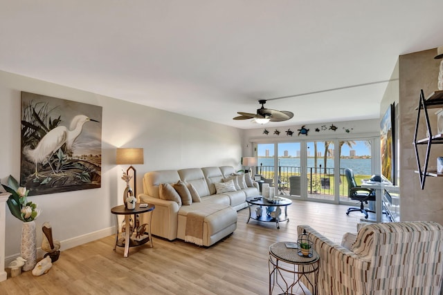 living room with light wood-type flooring, a water view, and ceiling fan