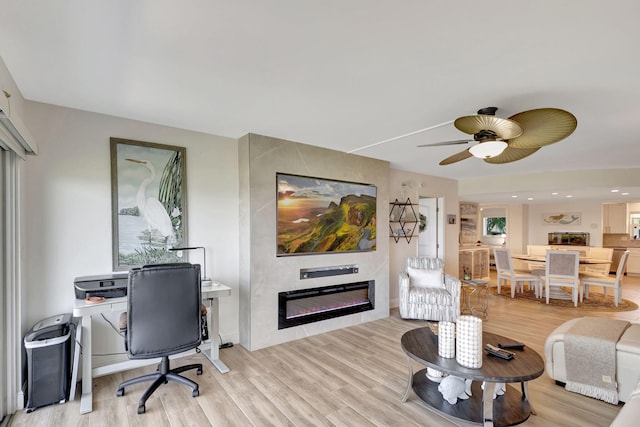 living room featuring ceiling fan, light hardwood / wood-style floors, and a large fireplace