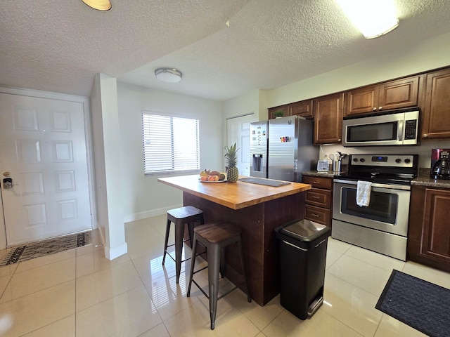 kitchen featuring wooden counters, stainless steel appliances, a kitchen bar, light tile patterned floors, and a textured ceiling