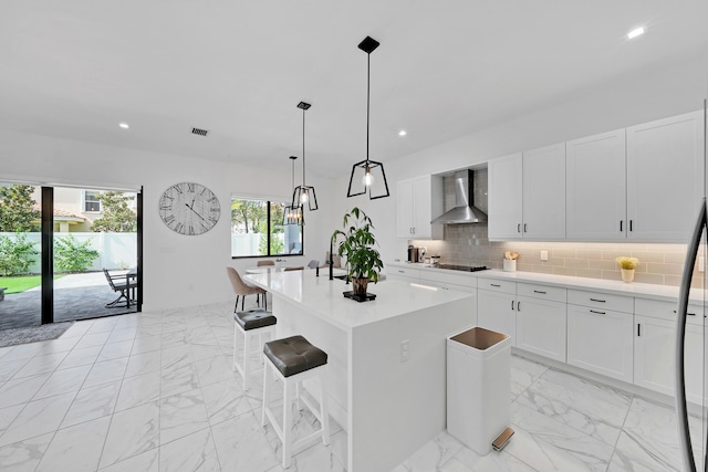 kitchen featuring black gas cooktop, white cabinetry, wall chimney range hood, backsplash, and a kitchen island with sink