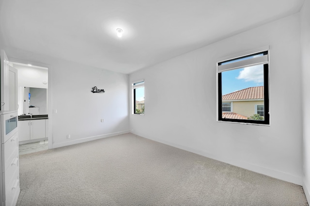 unfurnished room featuring sink, light carpet, and plenty of natural light