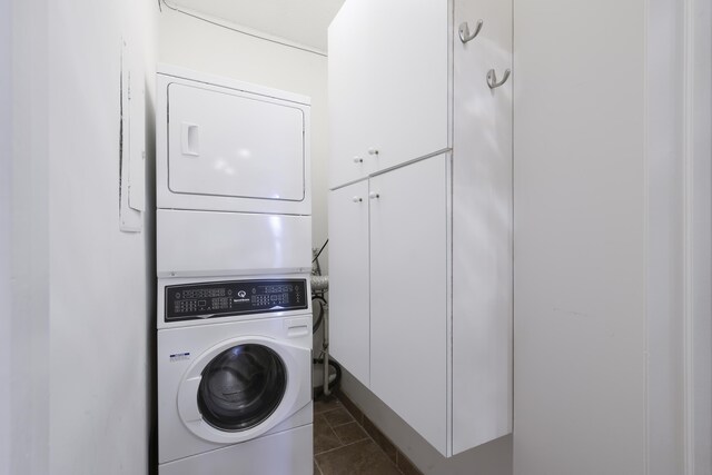 laundry area featuring cabinets, dark tile patterned flooring, and stacked washer and clothes dryer