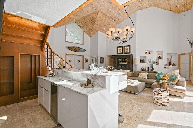 kitchen with a kitchen island, wood ceiling, a notable chandelier, light stone counters, and high vaulted ceiling