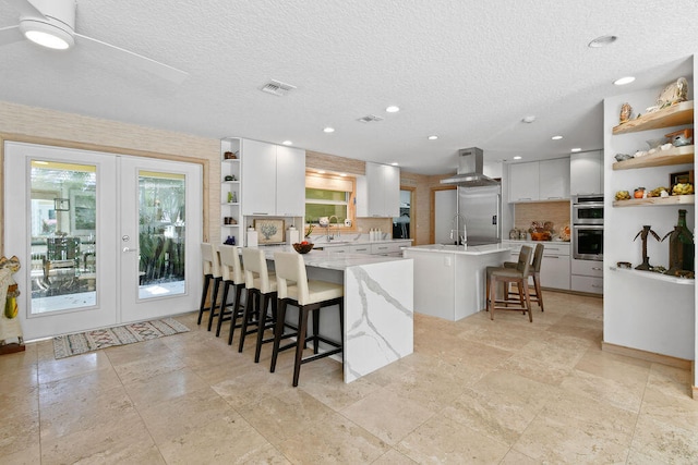 kitchen featuring a kitchen island, a textured ceiling, white cabinetry, a breakfast bar area, and ventilation hood