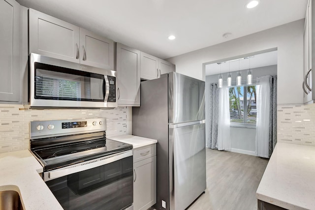 kitchen featuring pendant lighting, stainless steel appliances, decorative backsplash, gray cabinets, and light hardwood / wood-style flooring