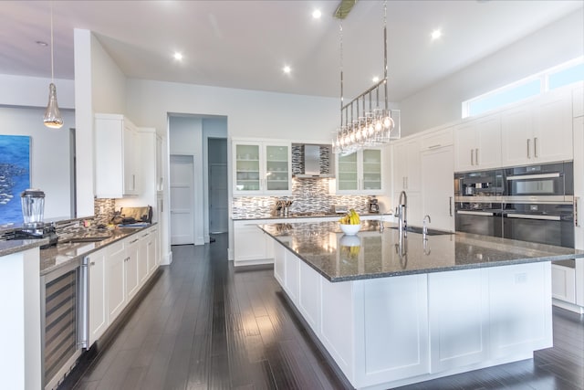 kitchen with wall chimney range hood, a large island, white cabinets, dark hardwood / wood-style floors, and sink