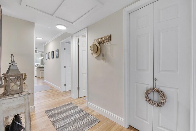 hall featuring attic access, light wood-style floors, crown molding, and baseboards