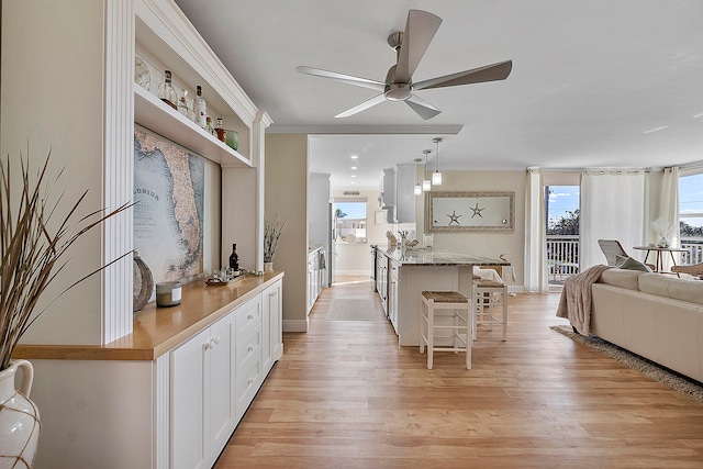 kitchen with ceiling fan, white cabinetry, a kitchen bar, pendant lighting, and light hardwood / wood-style floors