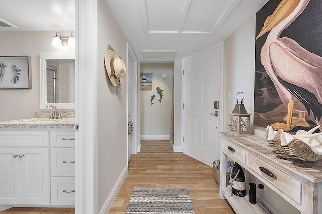 mudroom featuring attic access, light wood-style flooring, a sink, visible vents, and baseboards