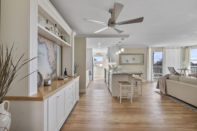 interior space featuring a breakfast bar, light wood-style floors, ceiling fan, and a healthy amount of sunlight