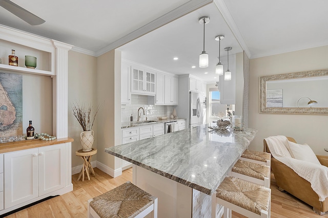 kitchen with light hardwood / wood-style flooring, hanging light fixtures, stainless steel appliances, a kitchen bar, and white cabinetry