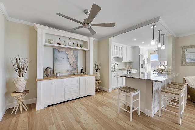 kitchen with stainless steel fridge, a kitchen bar, light wood finished floors, and ornamental molding