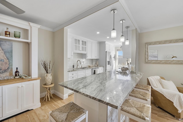 kitchen with a sink, light wood-style floors, stainless steel appliances, white cabinets, and light stone countertops