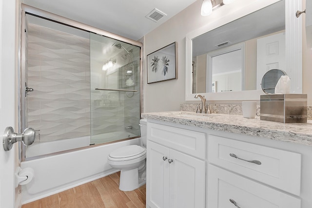 full bathroom with vanity, hardwood / wood-style floors, bath / shower combo with glass door, and toilet