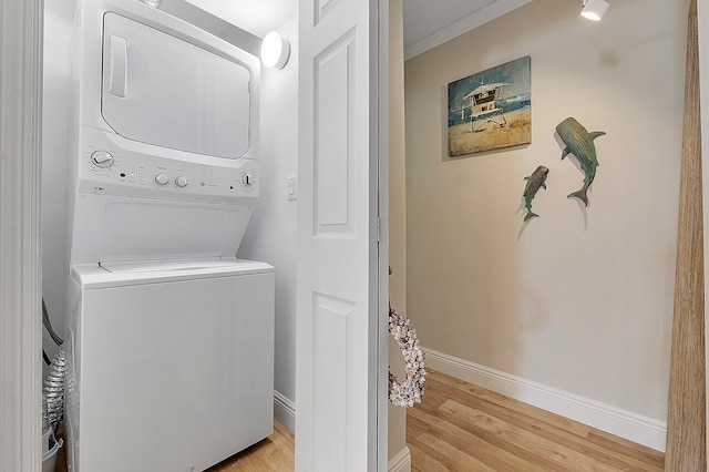 washroom with ornamental molding, stacked washer and clothes dryer, and light hardwood / wood-style floors