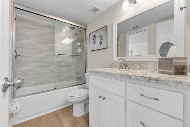 full bathroom with wood finished floors, vanity, visible vents, toilet, and shower / bath combination with glass door