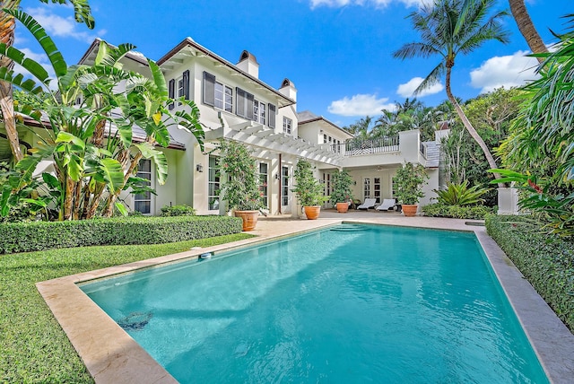 rear view of house with a fenced in pool, a patio area, french doors, and a balcony