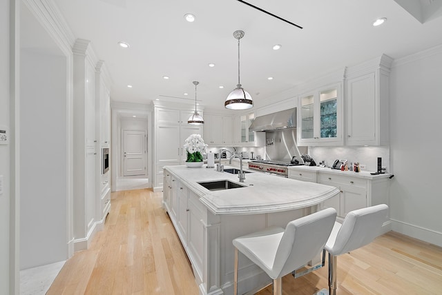 kitchen with white cabinetry, wall chimney range hood, and a kitchen island with sink