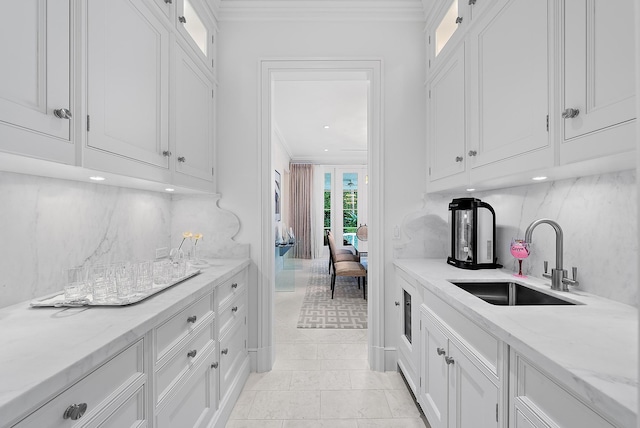 kitchen with backsplash, ornamental molding, sink, light stone countertops, and white cabinets