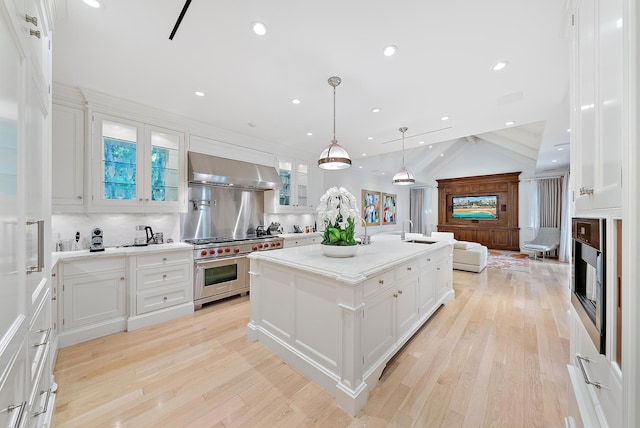 kitchen featuring premium stove, white cabinets, a kitchen island with sink, and range hood