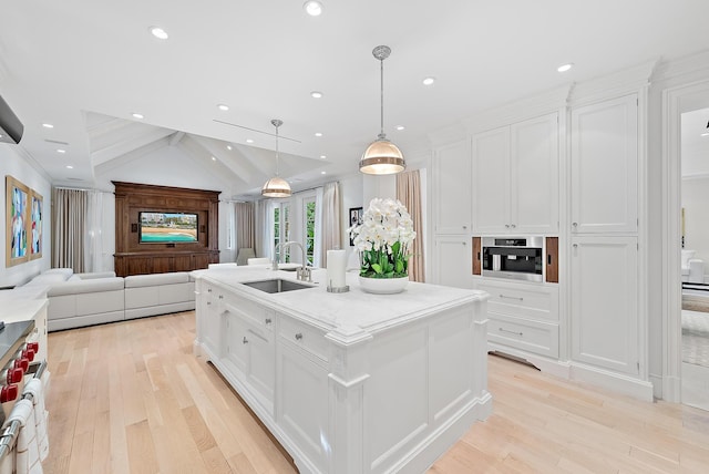 kitchen with white cabinets, a kitchen island with sink, vaulted ceiling with beams, light hardwood / wood-style floors, and sink