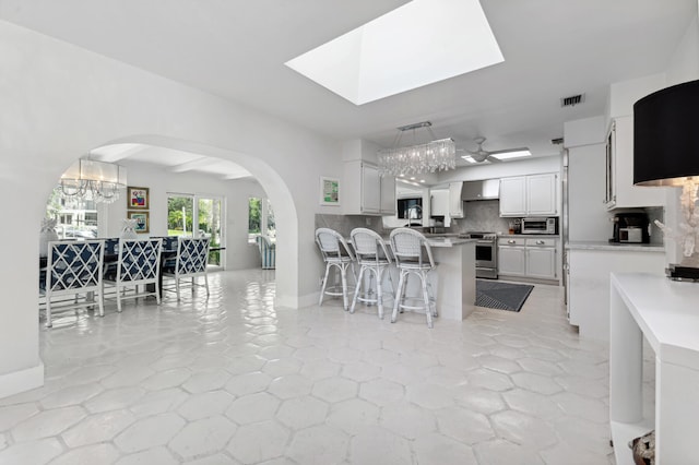 kitchen with a kitchen breakfast bar, white cabinetry, stainless steel electric stove, hanging light fixtures, and decorative backsplash