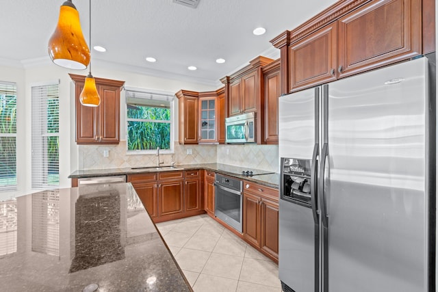 kitchen featuring dark stone counters, sink, hanging light fixtures, ornamental molding, and stainless steel appliances