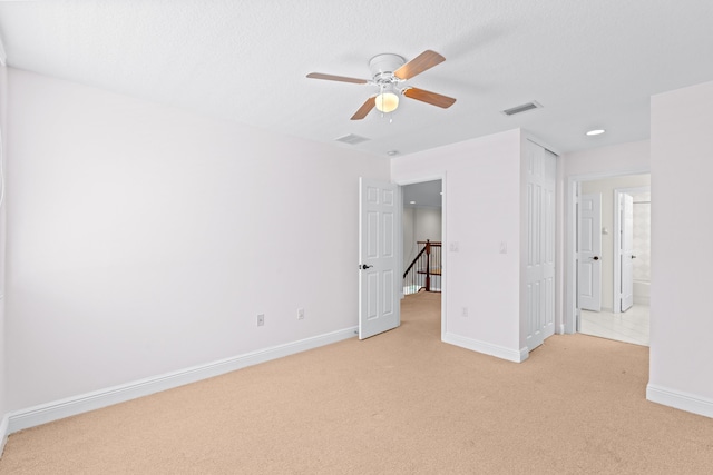 unfurnished bedroom with ensuite bath, ceiling fan, light carpet, and a textured ceiling