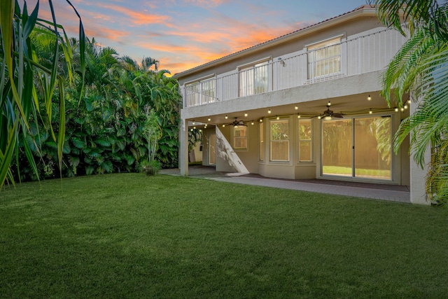 back house at dusk with ceiling fan and a yard