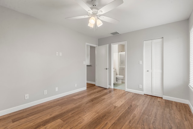 unfurnished bedroom with a closet, ensuite bath, wood-type flooring, and ceiling fan