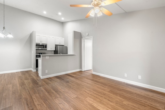 kitchen featuring white cabinetry, light hardwood / wood-style flooring, ceiling fan with notable chandelier, a towering ceiling, and stainless steel appliances