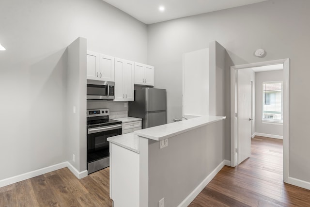 kitchen with white cabinetry, appliances with stainless steel finishes, kitchen peninsula, and dark hardwood / wood-style floors