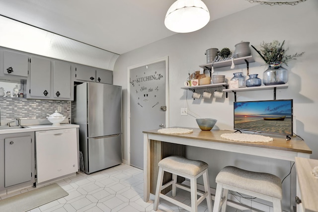 kitchen with decorative backsplash, stainless steel fridge, dishwasher, gray cabinets, and a breakfast bar area