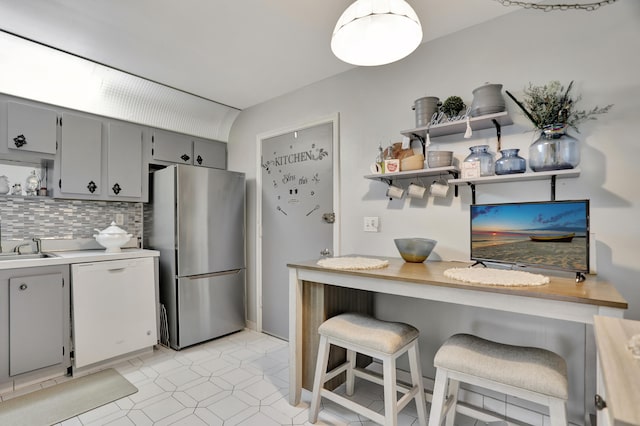 kitchen featuring gray cabinetry, dishwasher, stainless steel fridge, tasteful backsplash, and a breakfast bar area