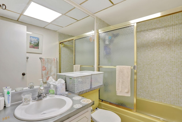 full bathroom featuring toilet, vanity, a drop ceiling, and shower / bath combination with glass door