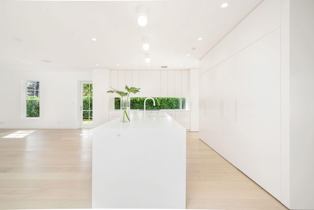 kitchen featuring a kitchen island with sink, light hardwood / wood-style floors, white cabinetry, and sink