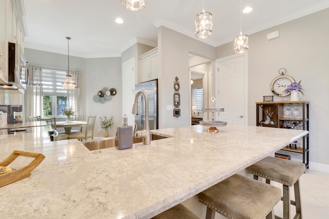 kitchen with ornamental molding, pendant lighting, light stone countertops, a breakfast bar, and white cabinets