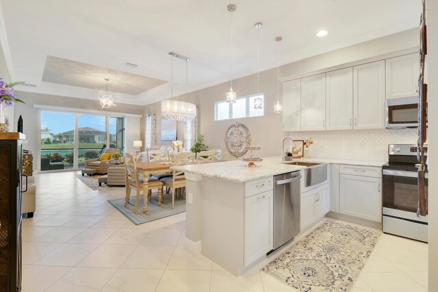 kitchen with stainless steel appliances, pendant lighting, sink, a tray ceiling, and white cabinetry