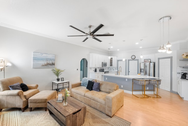 living room with crown molding, sink, light wood-type flooring, and ceiling fan