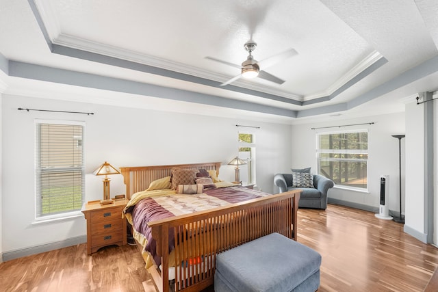 bedroom featuring light hardwood / wood-style flooring, a tray ceiling, crown molding, and ceiling fan