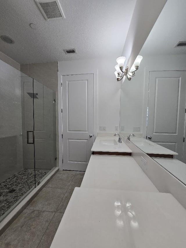 full bathroom featuring double vanity, visible vents, a stall shower, a sink, and a textured ceiling