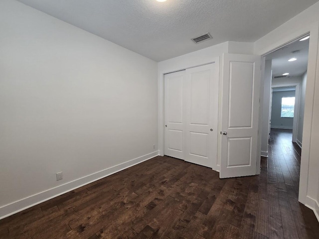 unfurnished bedroom featuring dark wood-style floors, a closet, visible vents, a textured ceiling, and baseboards