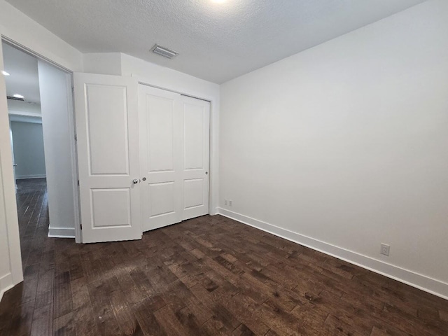 unfurnished bedroom with dark wood-style flooring, a closet, visible vents, a textured ceiling, and baseboards