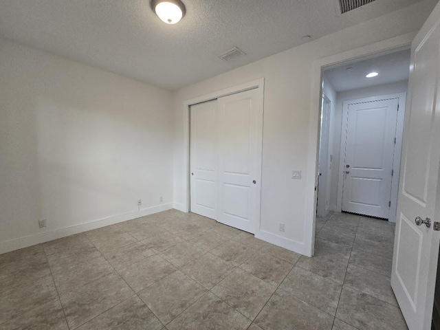 unfurnished bedroom with a closet, visible vents, a textured ceiling, and baseboards