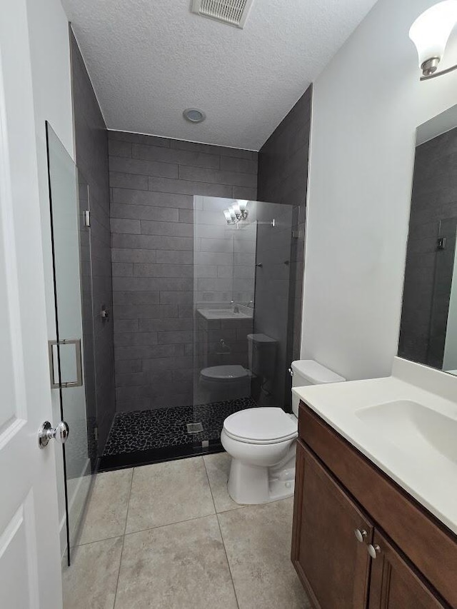 full bath with a textured ceiling, toilet, vanity, visible vents, and a tile shower