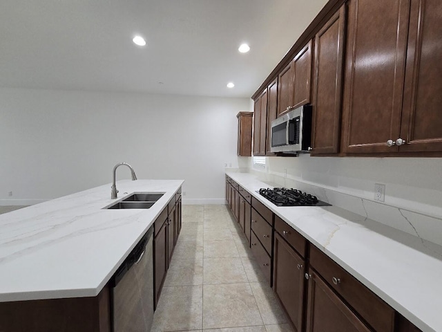 kitchen featuring light stone countertops, stainless steel appliances, dark brown cabinets, a sink, and recessed lighting